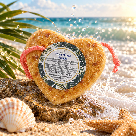 Heart-shaped peach mango soap in a sponge bar wrapped in clear plastic with a pink drawstring and a round product label, shown on a plain white background.
